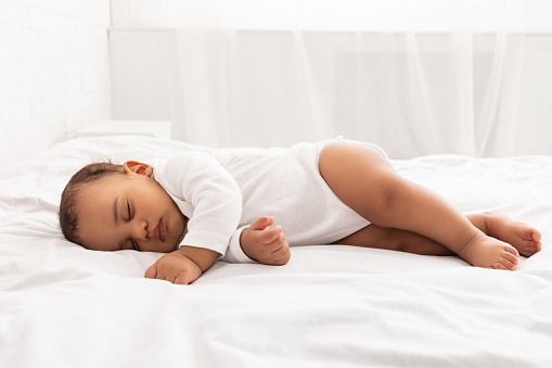 Cute Little Baby Sleeping Lying On Side In Bed In Bedroom At Home, With Eyes Closed. Peaceful Toddler Child Napping Resting During Daytime Sleep Indoors. Side-View Shot